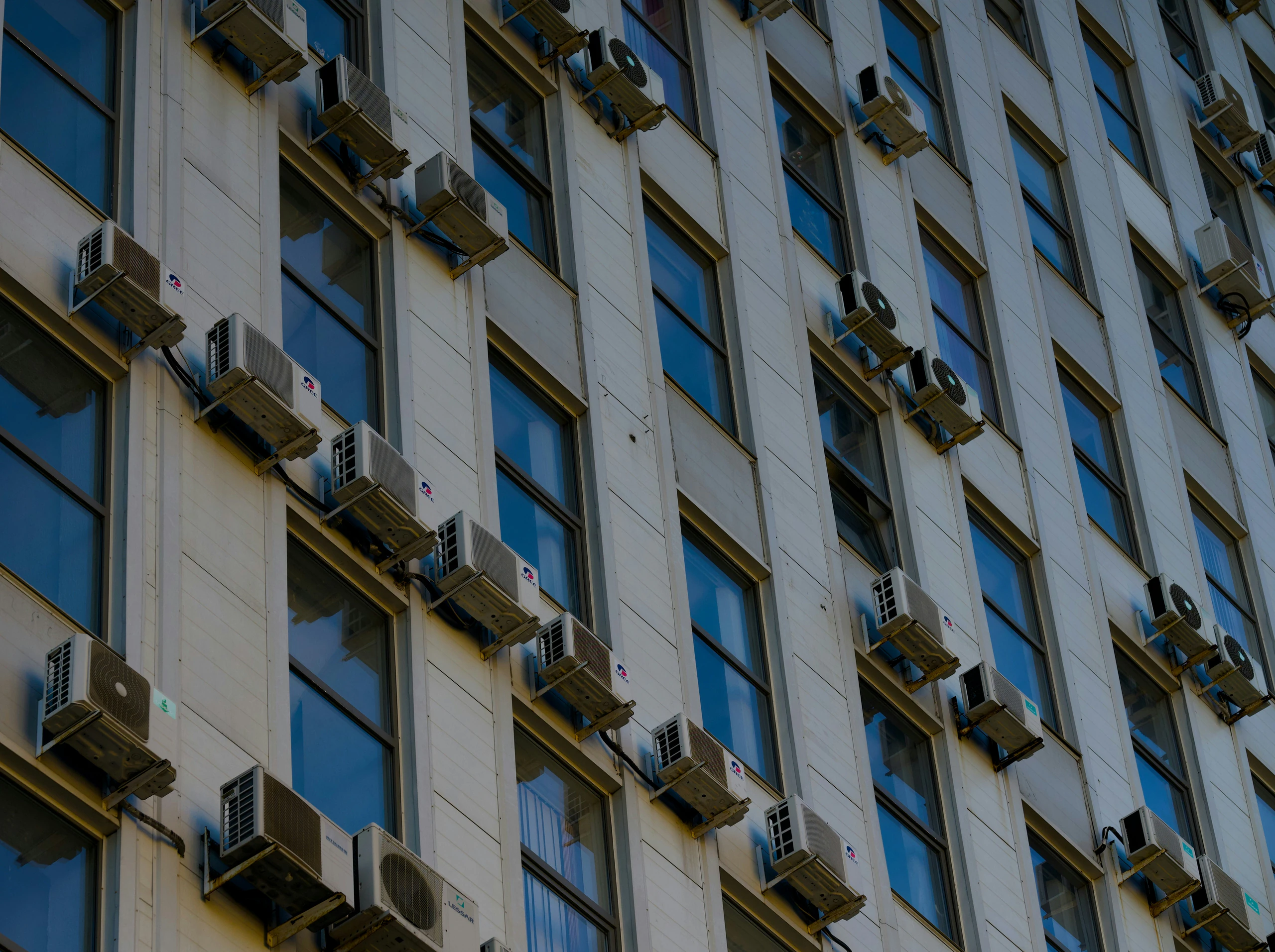 Building facade lined with multiple wall-mounted split AC condenser units for commercial HVAC