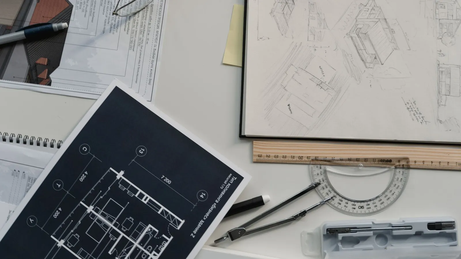Architectural sketches, a ruler and a dark-background floor plan laid out on a white desk