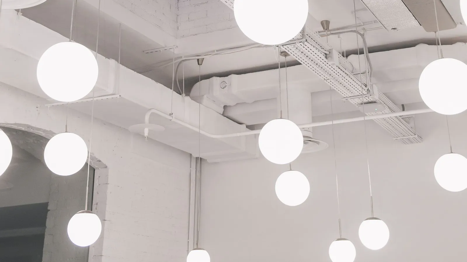 White globe pendant lights hanging below a white ceiling with exposed cable tray and ductwork