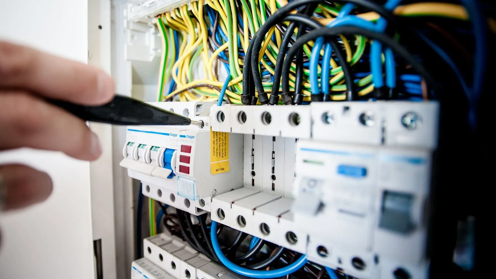 Distribution board with circuit breakers and coloured wiring, a hand pointing with a pen