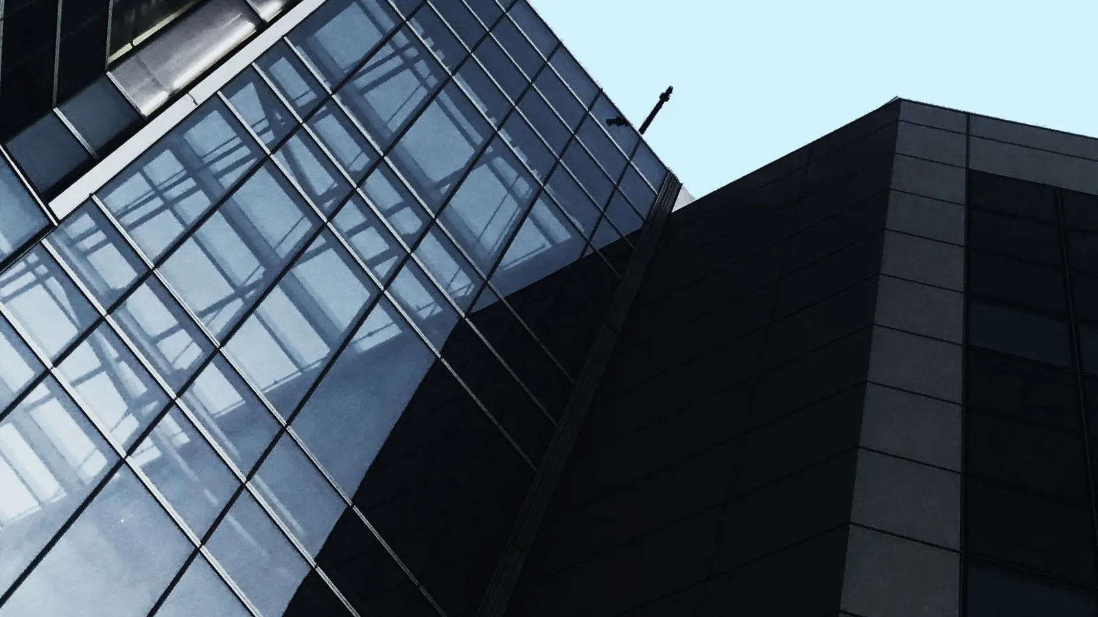 Glass and dark-panel office towers seen from below against a pale sky