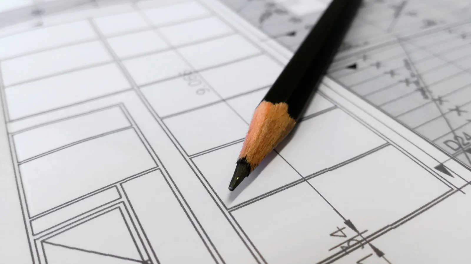 Sharp black pencil resting on a ruled architectural plan drawing