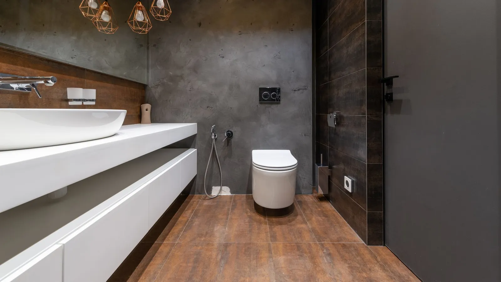 Washroom with a white floating vanity, wall-hung toilet and copper pendant lights on a concrete-effect wall
