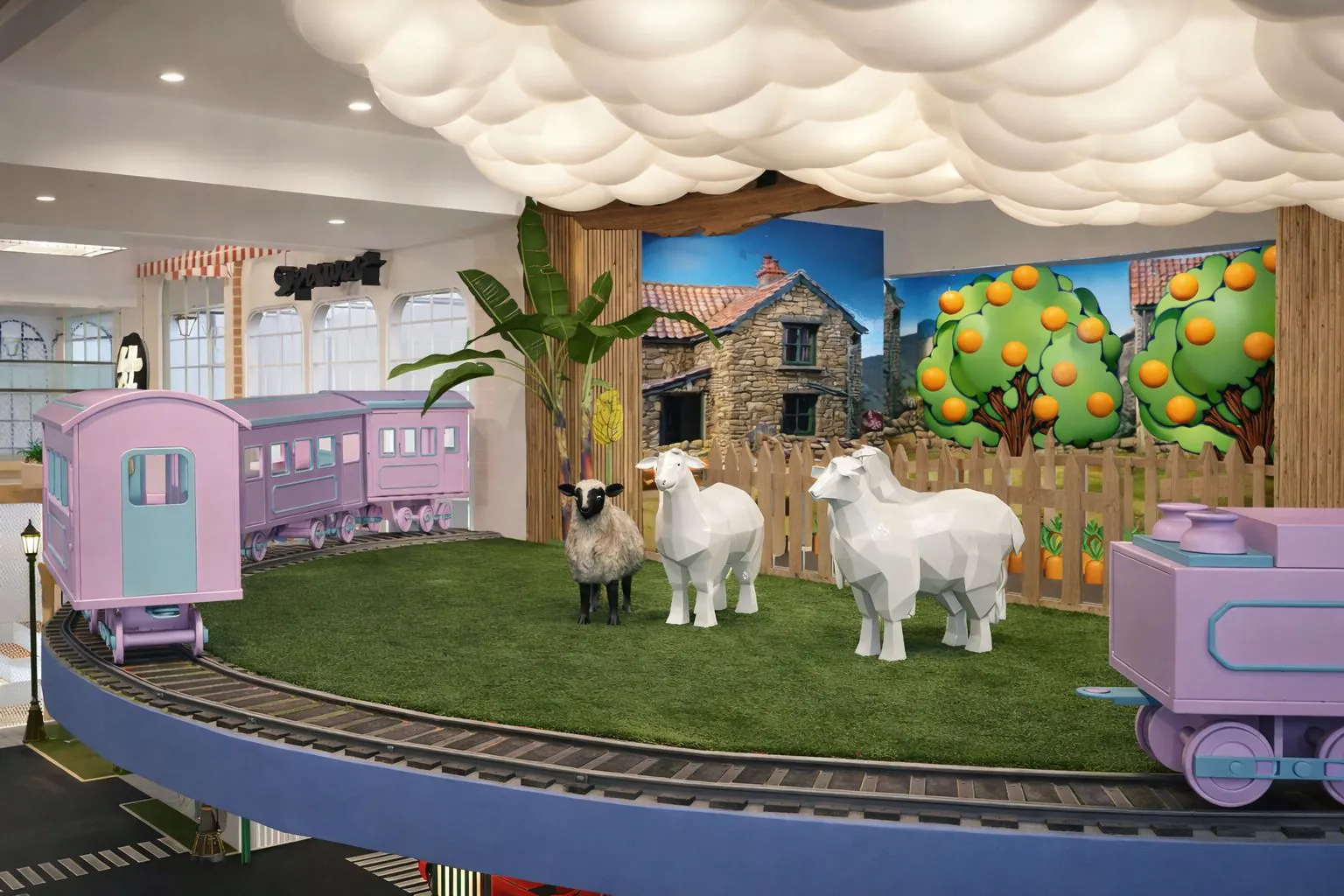 Indoor play farm with model sheep, a fruit tree mural and a train carriage alongside