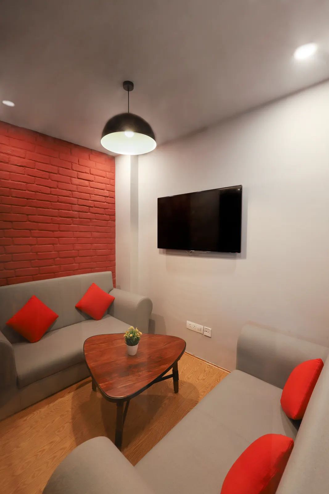 Hashtag Orange lounge with a grey sofa, orange cushions and a red brick feature wall
