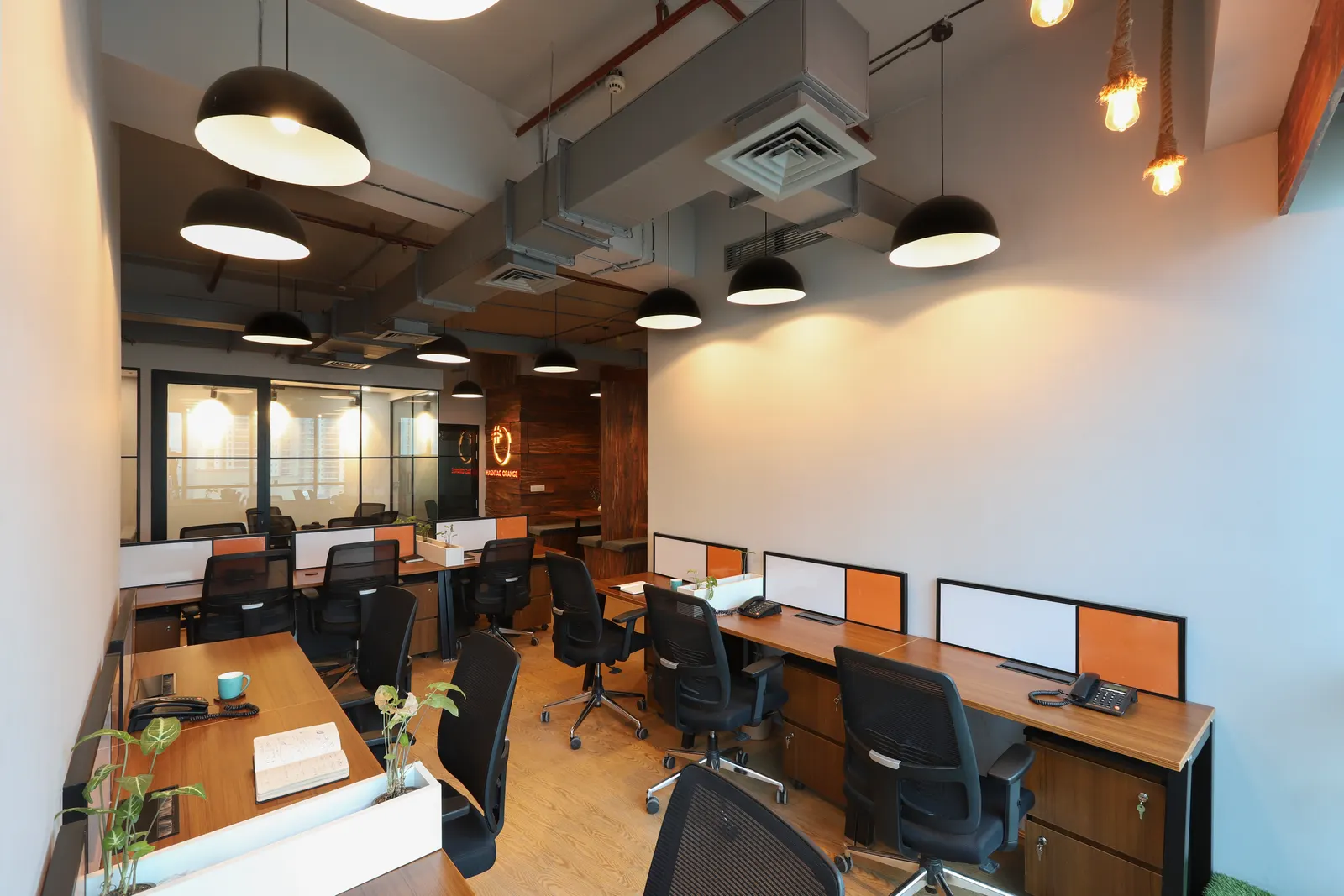 Hashtag Orange open office in Gurugram with black dome pendant lights, timber flooring and glass-partitioned cabins