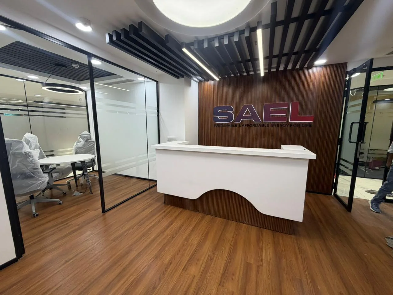 SAEL office reception desk with wood-panel signage wall and adjoining glazed meeting room