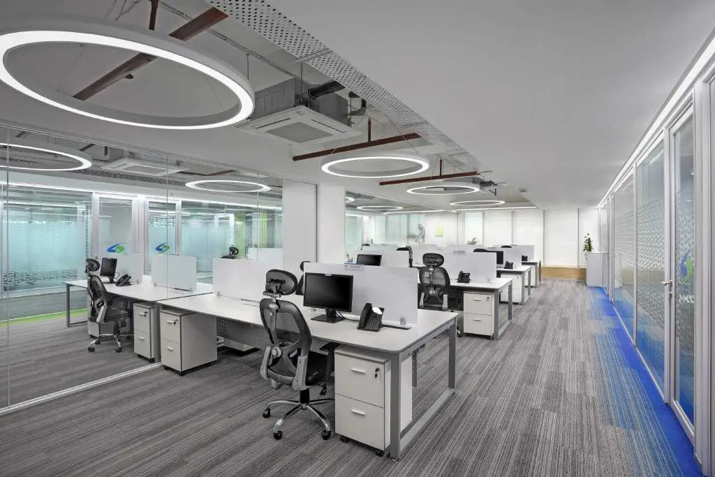 Synergy Consulting open office with white workstations under large ring pendant lights beside glass cabins
