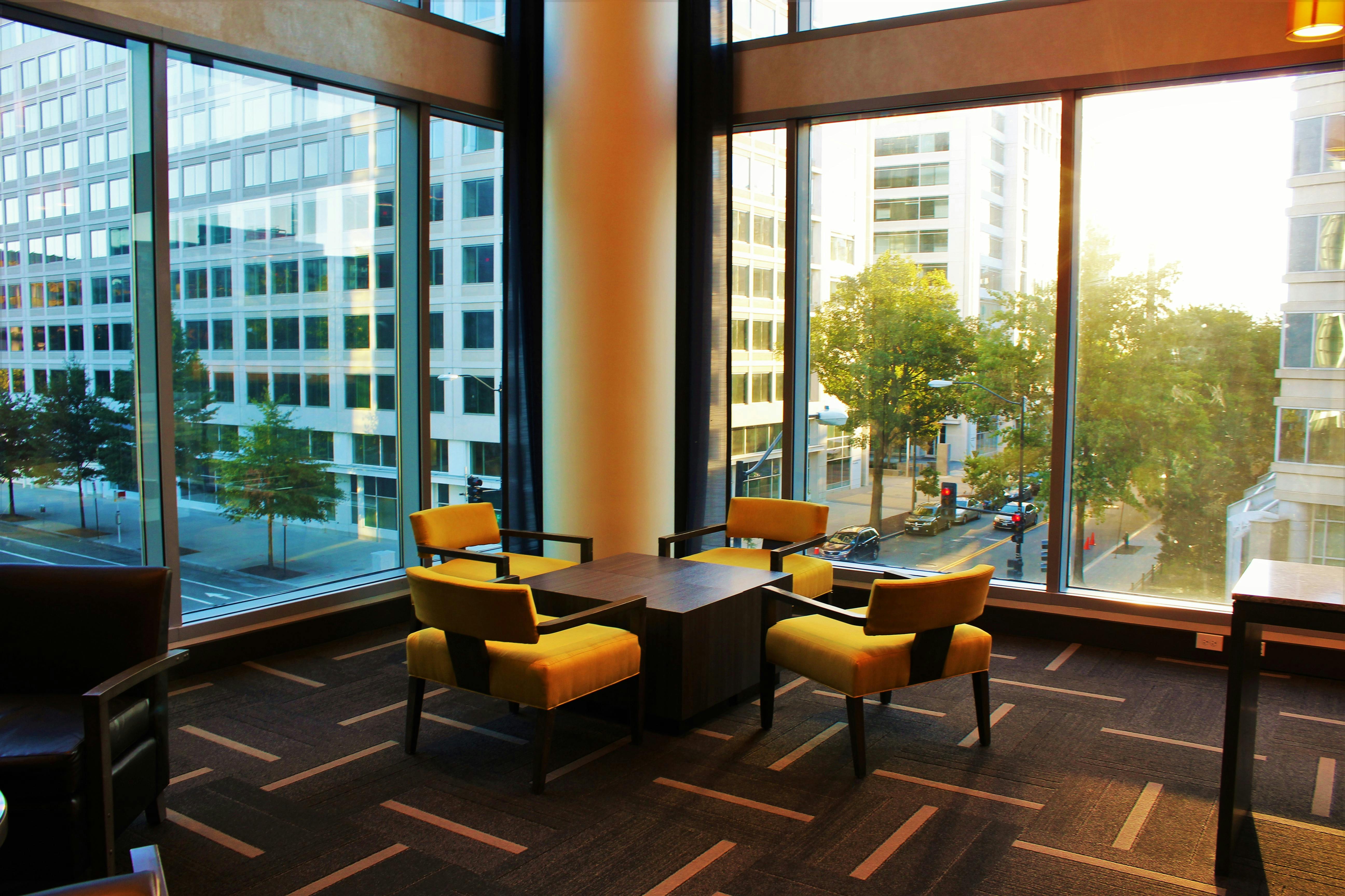 Contemporary hotel lounge featuring yellow chairs and cityscape view through large windows.